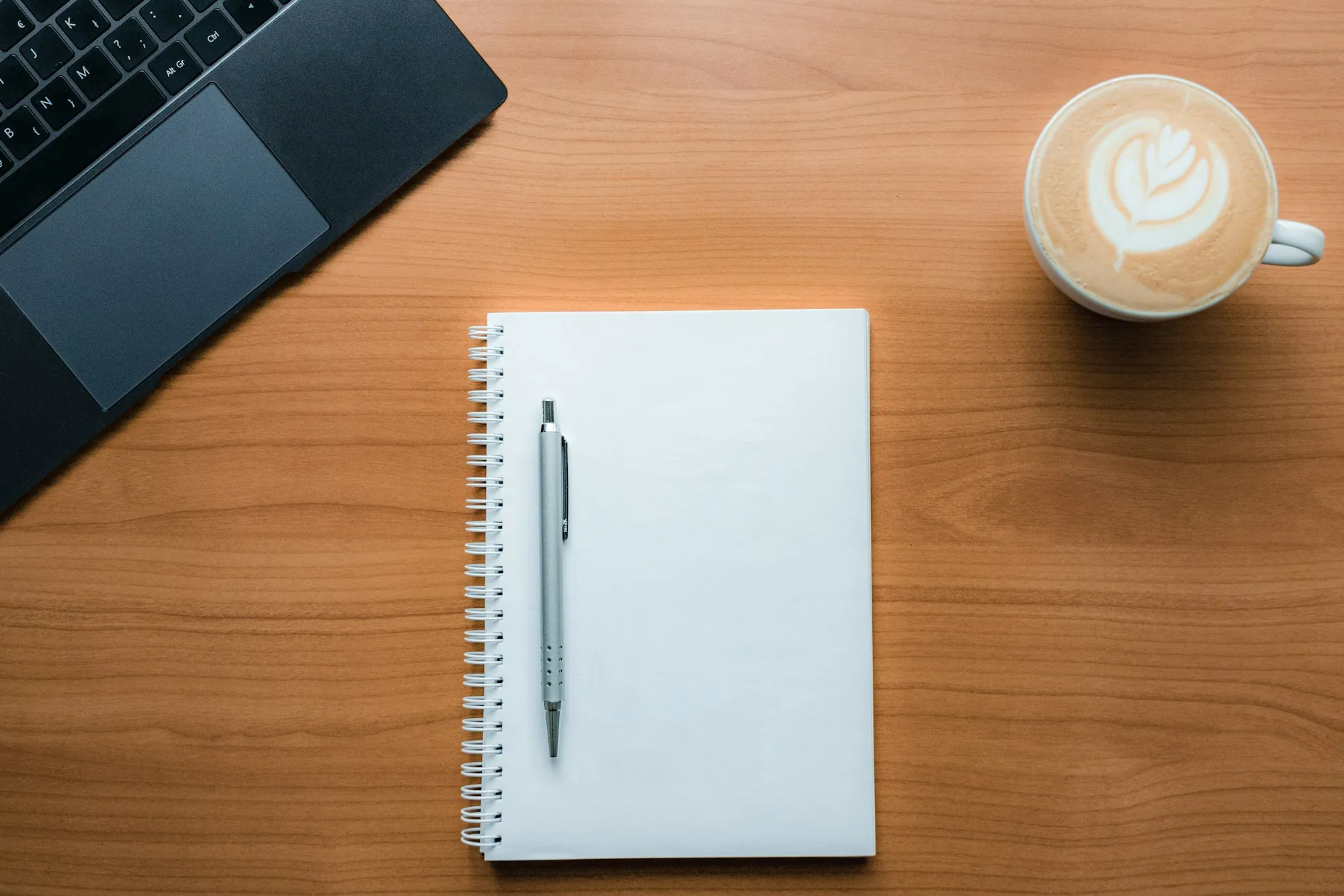 A notebook, pen and coffee cup on a desk