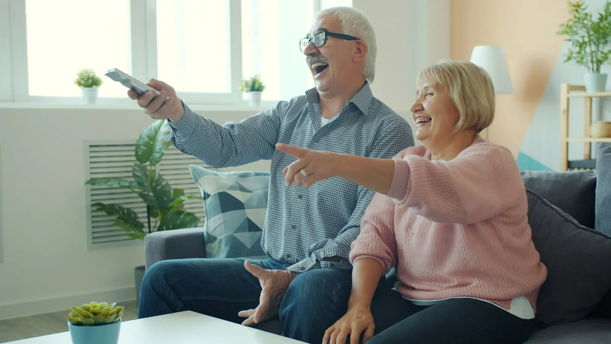 An older couple laughing together on the sofa at home