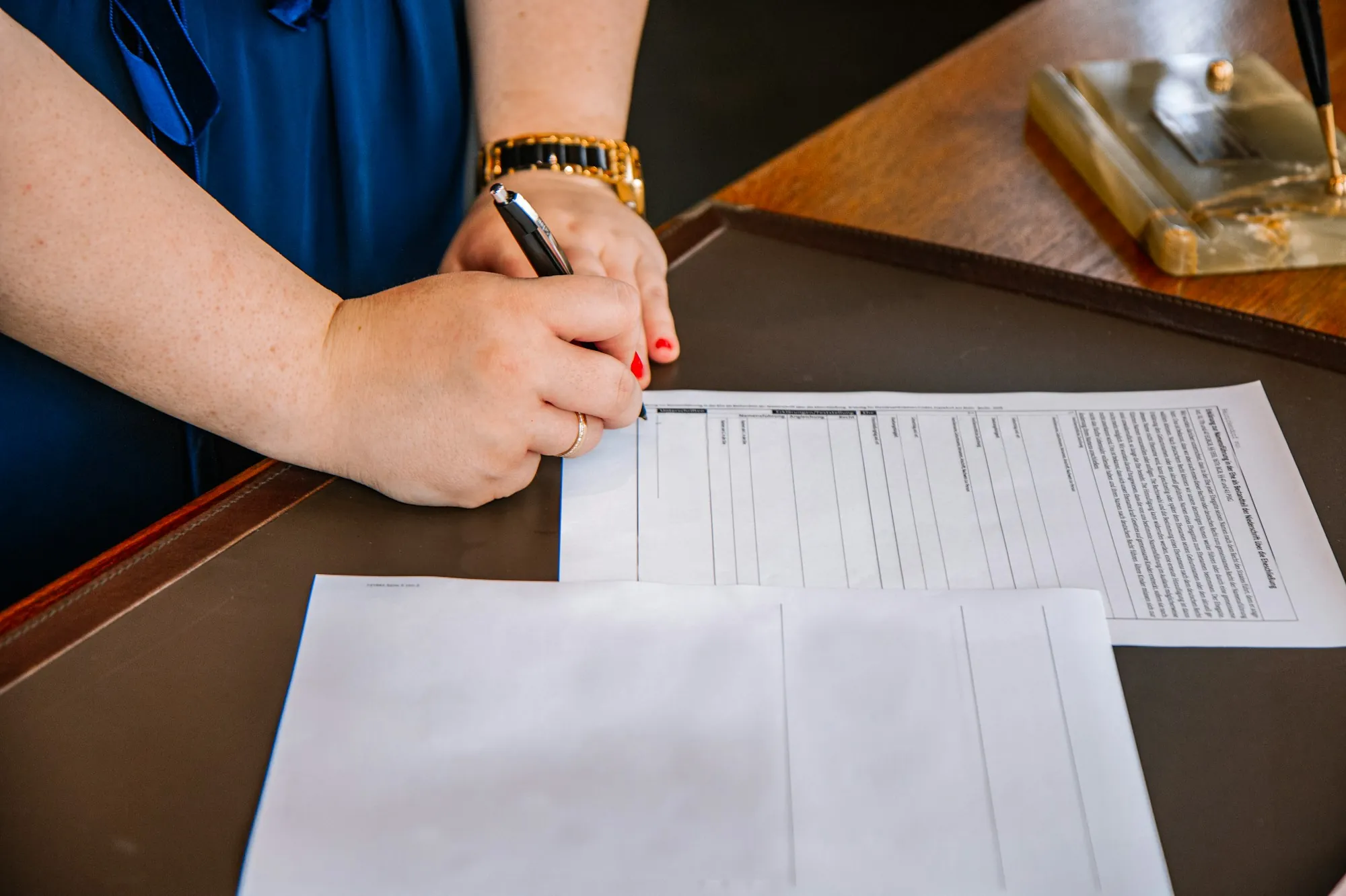 A hand filling in a printed form at a desk