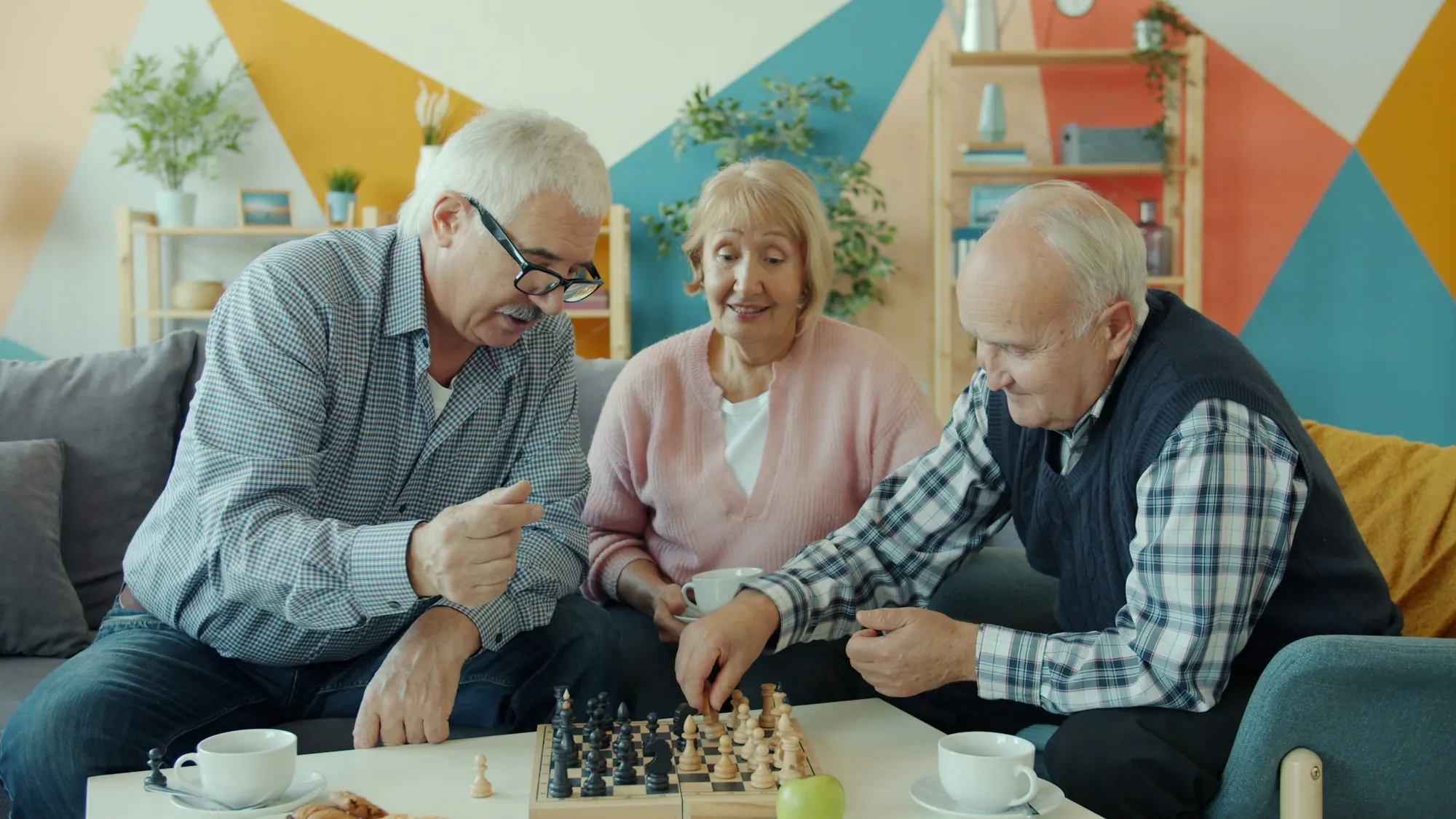 Three older people playing chess together in a living room