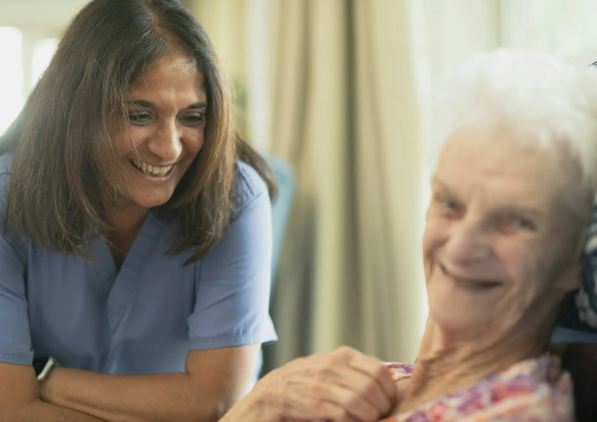 A home health aide sitting beside an older woman in her living room